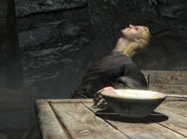 A screenshot from Skyrim. The dead body of a mage slumps in a chair, his hand still resting on the table next to him.