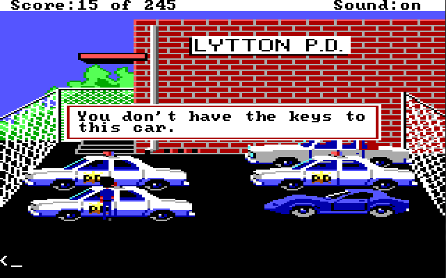 The police station parking lot. The police station is a large red brick building in the background with a sign that says "LYTTON PD." There are three cop cars, a white car, and a flashy blue car parked in the lot. Sonny stands next to one of the cop cars. Game text reads, "You don't have the keys to this car."