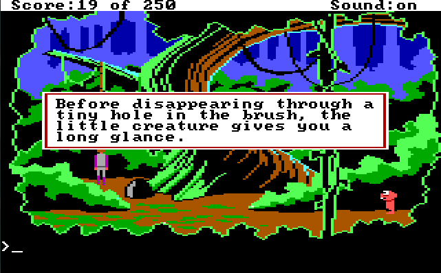 A forest area with one large tree in the center, with vines hanging from its branches. Roger stands by the tree, and a small pink alien stands on the opposite side of the screen looking at him. Game text: "Before disappearing through a tiny hole in the brush, the little creature gives you a long glance."