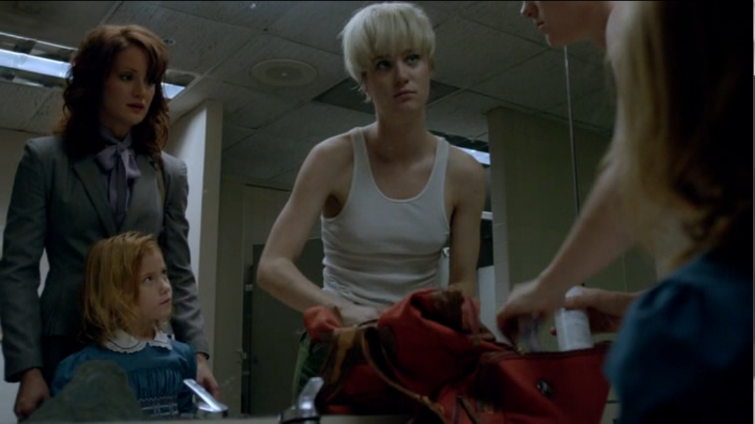 Still from Halt and Catch Fire. Two women and a little girl stand in front of a public bathroom mirror. On the left is Donna, in a prim business suit, and her young daughter. Both are staring at Cameron on the right, who is wearing only a tank top and cargo pants and is rooting through a red duffle bag on the counter. 