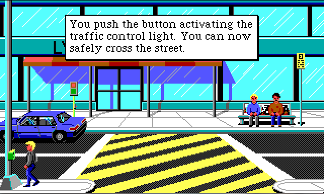 The front of a large, glass-walled building. There is a road running in front of it with a large yellow-striped pedestrian crossing in the middle. Sonny stands on the near side of the road next to a pedestrian crossing button. Two men set on a bench across the road. Game text reads: "You push the button activating the traffic control light. You can now safely cross the street."